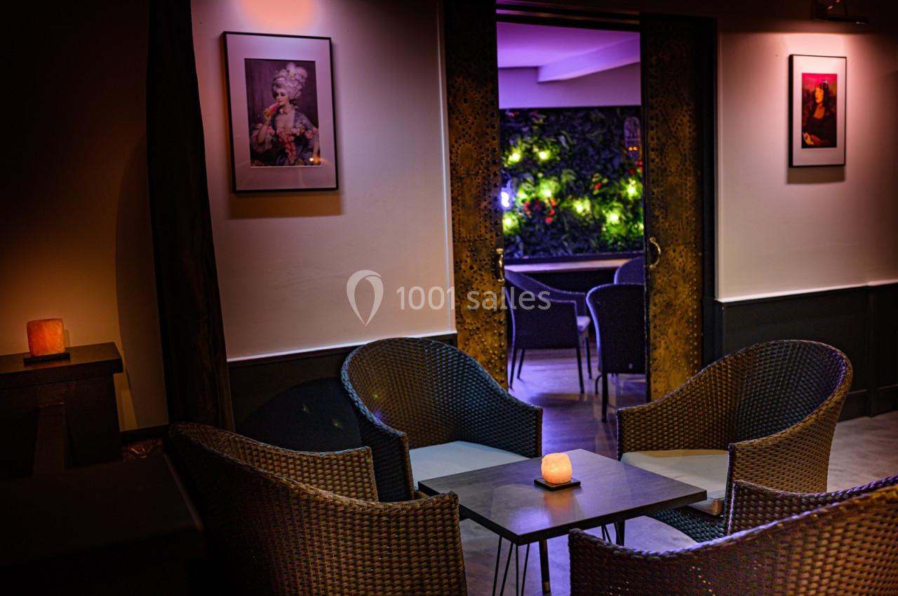 Espace lounge avec fauteuils en rotin, table basse et éclairage tamisé, donnant sur une terrasse végétalisée.