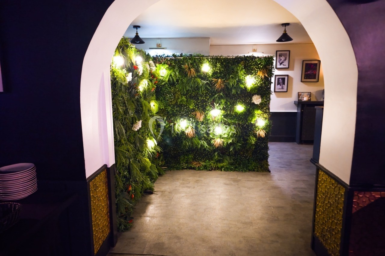 Mur végétal illuminé dans une pièce intérieure avec un sol en carrelage gris et un éclairage tamisé.