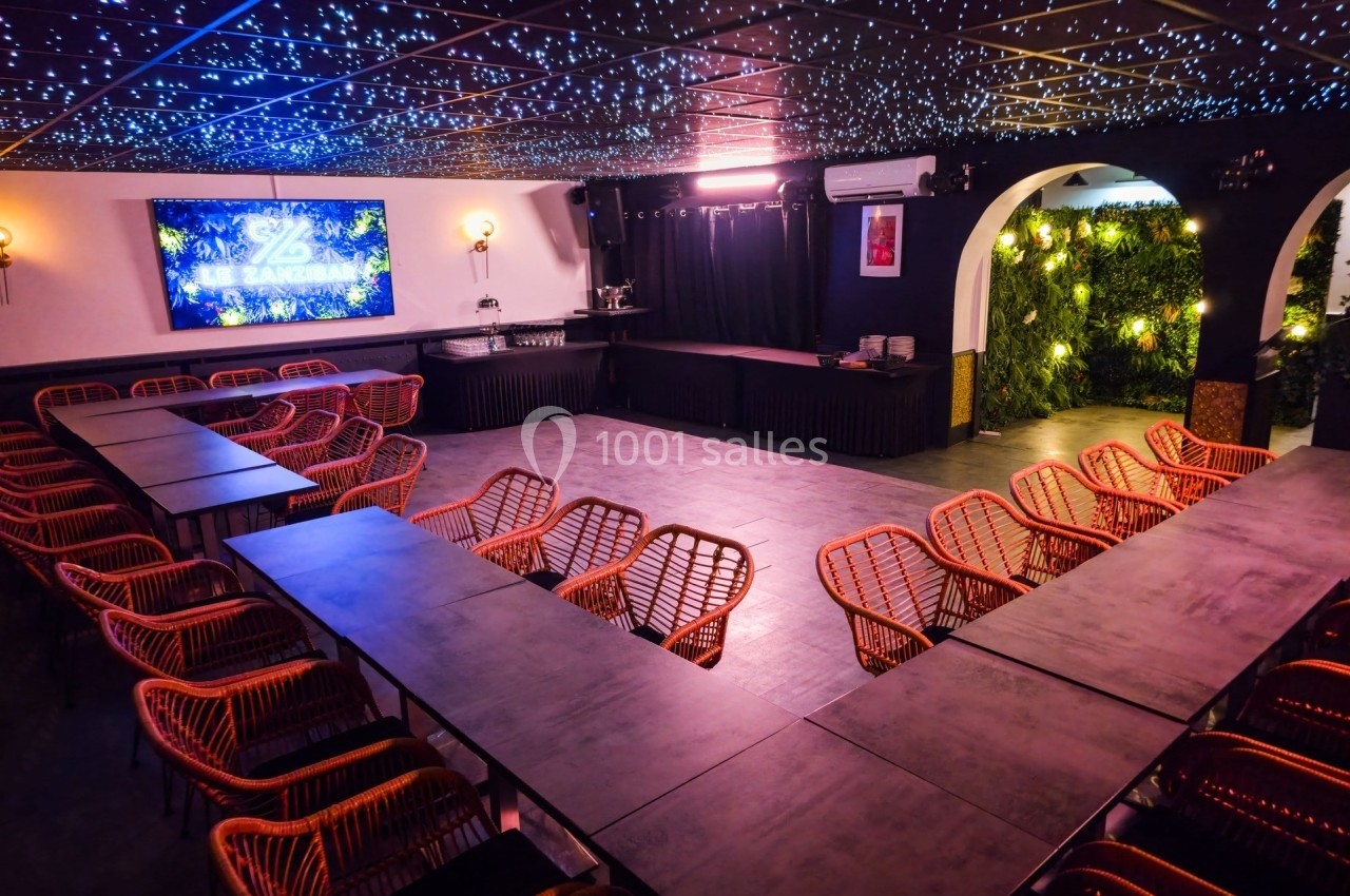 Salle de réunion avec tables disposées en U, chaises en rotin, éclairage tamisé et mur végétal en arrière-plan.