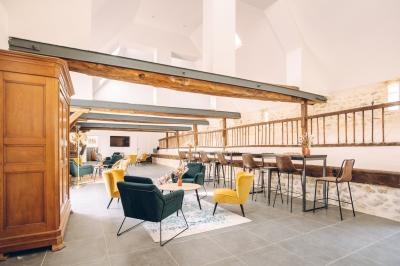 Des tables et chaises jaunes sont disposées sur une terrasse en plein air, près d'un arbre et d'un bâtiment clair.