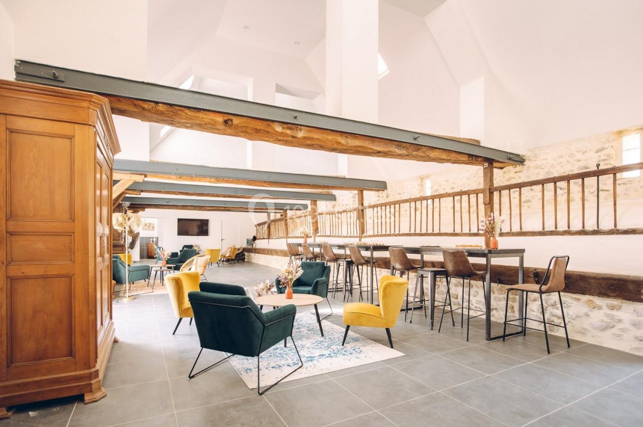 Salle lumineuse avec poutres apparentes, mobilier moderne et espace détente comprenant fauteuils, tables et un bar.