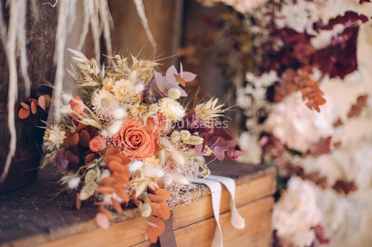 Bouquet de fleurs séchées aux tons chauds, posé sur une surface en bois, avec un fond flou de végétation.
