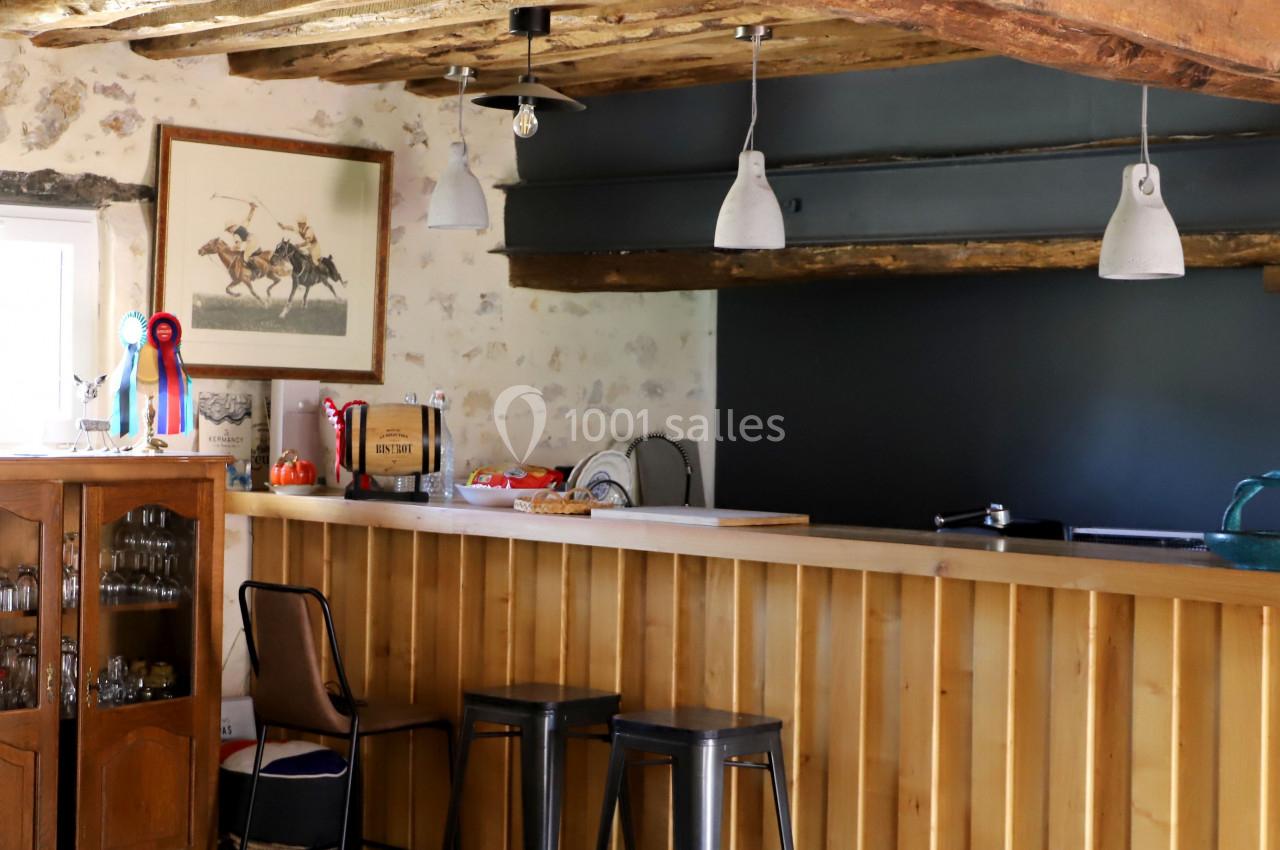 Cuisine rustique avec poutres apparentes, comptoir en bois, tabourets hauts et décoration équestre sur le mur.