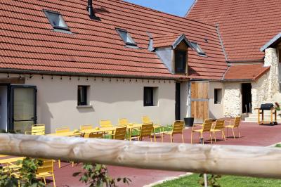 Des tables et chaises jaunes sont disposées sur une terrasse en plein air, près d'un arbre et d'un bâtiment clair.