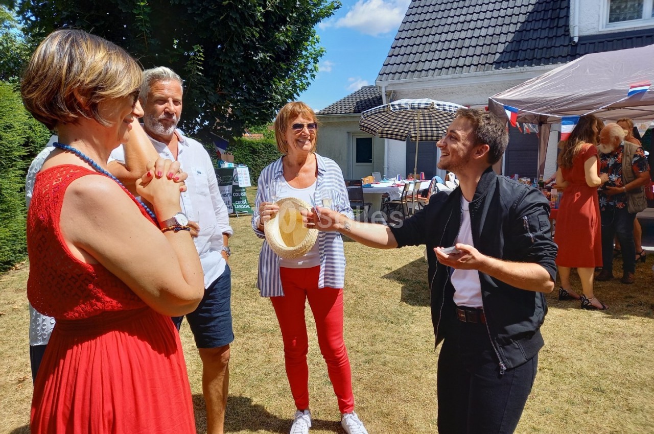 Un magicien réalise un tour devant un petit groupe de personnes souriantes lors d'un événement en extérieur.