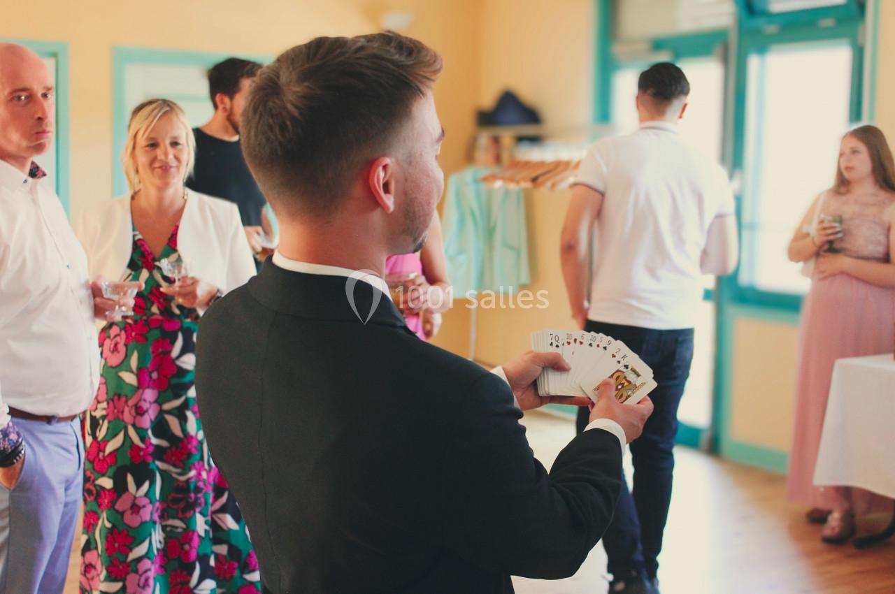 Un homme en costume réalise un tour de cartes devant un petit groupe de personnes dans une salle lumineuse.