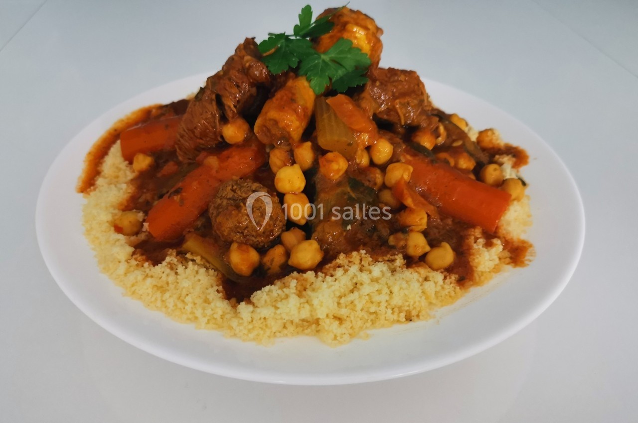Plat de couscous garni de légumes, pois chiches, boulettes et viande, présenté dans une assiette blanche.