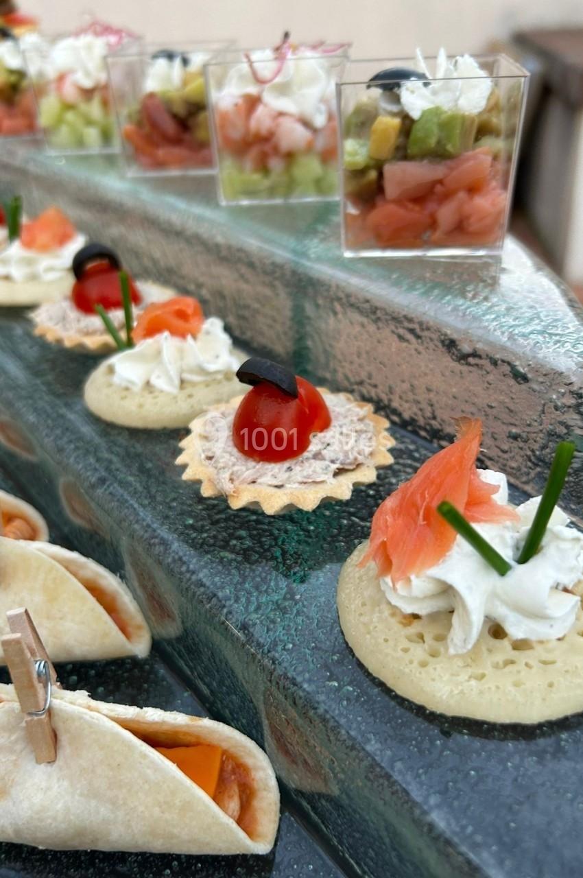 Assortiment de bouchées apéritives variées, incluant verrines, mini-tacos et canapés garnis de saumon et fromage.