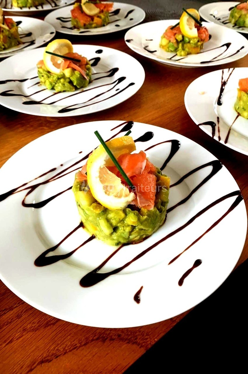Assiette contenant un tartare d'avocat et saumon fumé, décoré de citron, ciboulette et filet de sauce balsamique.