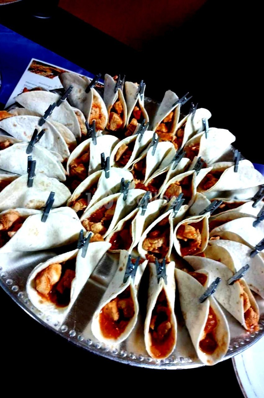 Plateau de mini-tacos garnis de viande et sauce, maintenus ouverts par des pinces, disposés en cercle.
