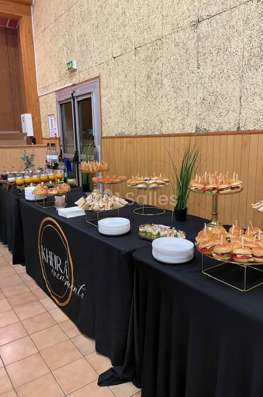 Buffet avec assortiments de sandwichs, verrines et boissons, disposé sur une table noire dans une salle en bois.