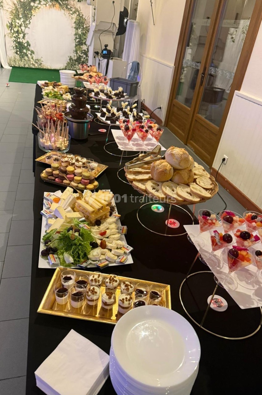 Buffet varié avec desserts, fromages, pains et fontaine de chocolat, disposé sur une longue table noire.