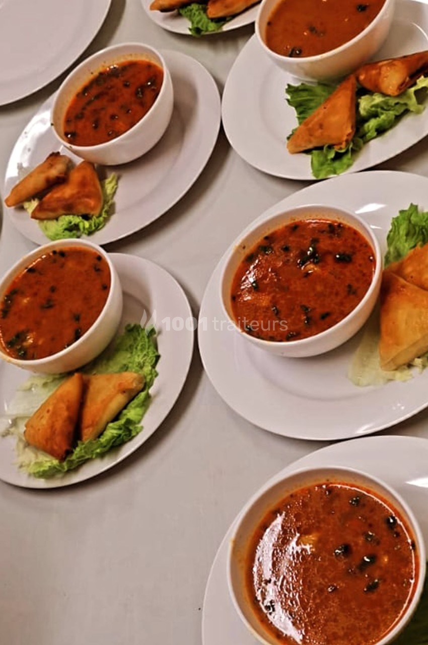 Assiettes contenant des bols de soupe épicée, accompagnées de samoussas sur des feuilles de salade.