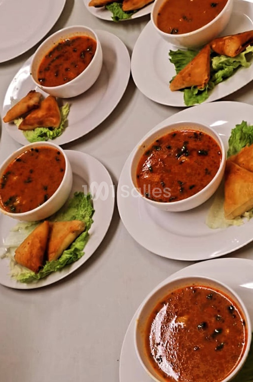 Assiettes contenant des bols de soupe épicée, accompagnées de samoussas sur des feuilles de salade.