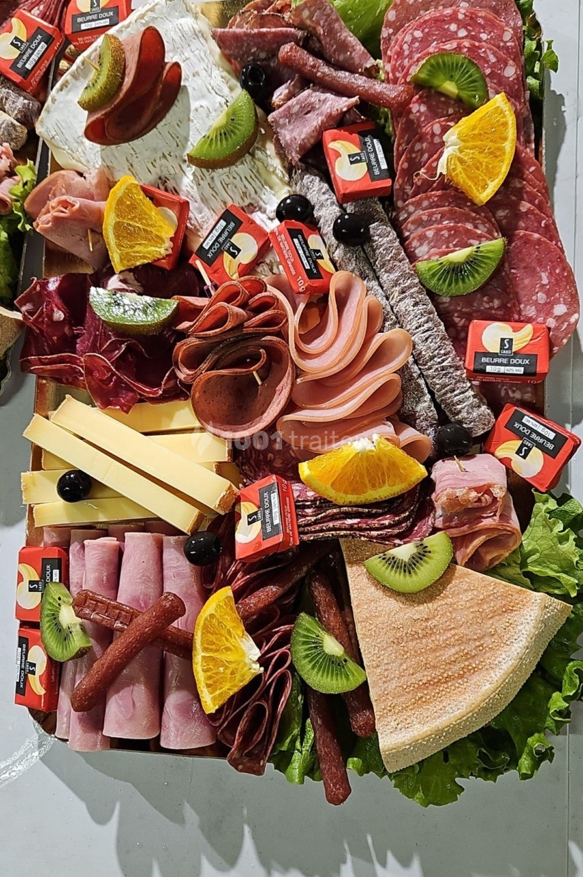 Plateau de charcuterie et fromages avec fruits frais, olives et tranches de pain, présenté sur un lit de salade verte.