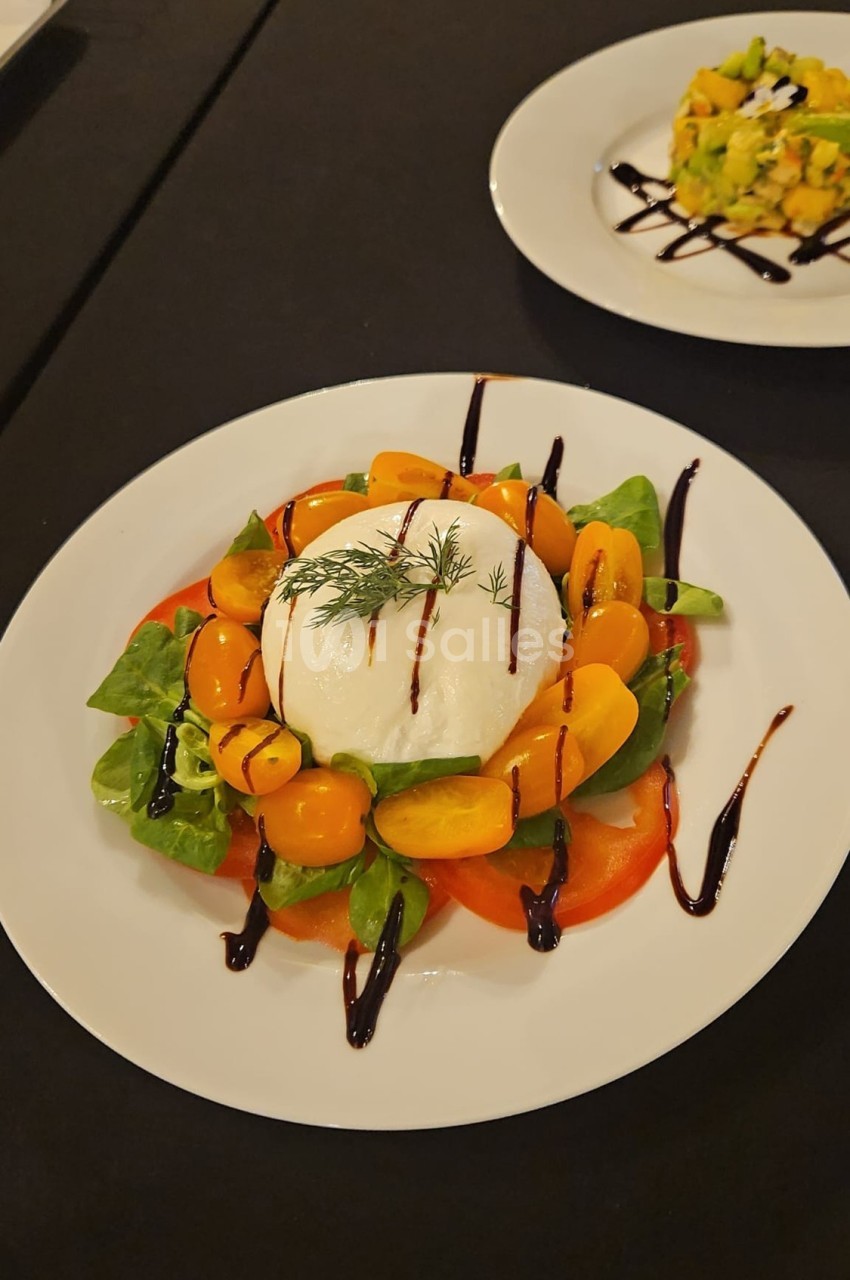 Assiette de burrata entourée de tomates cerises jaunes, salade verte et filet de vinaigre balsamique.