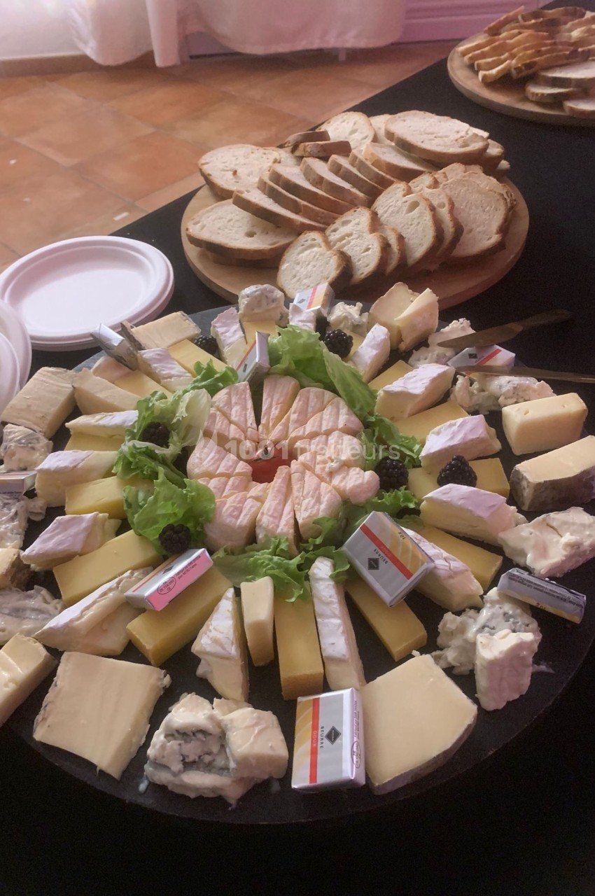 Plateau de fromages variés disposés en cercle avec des tranches de pain en arrière-plan.