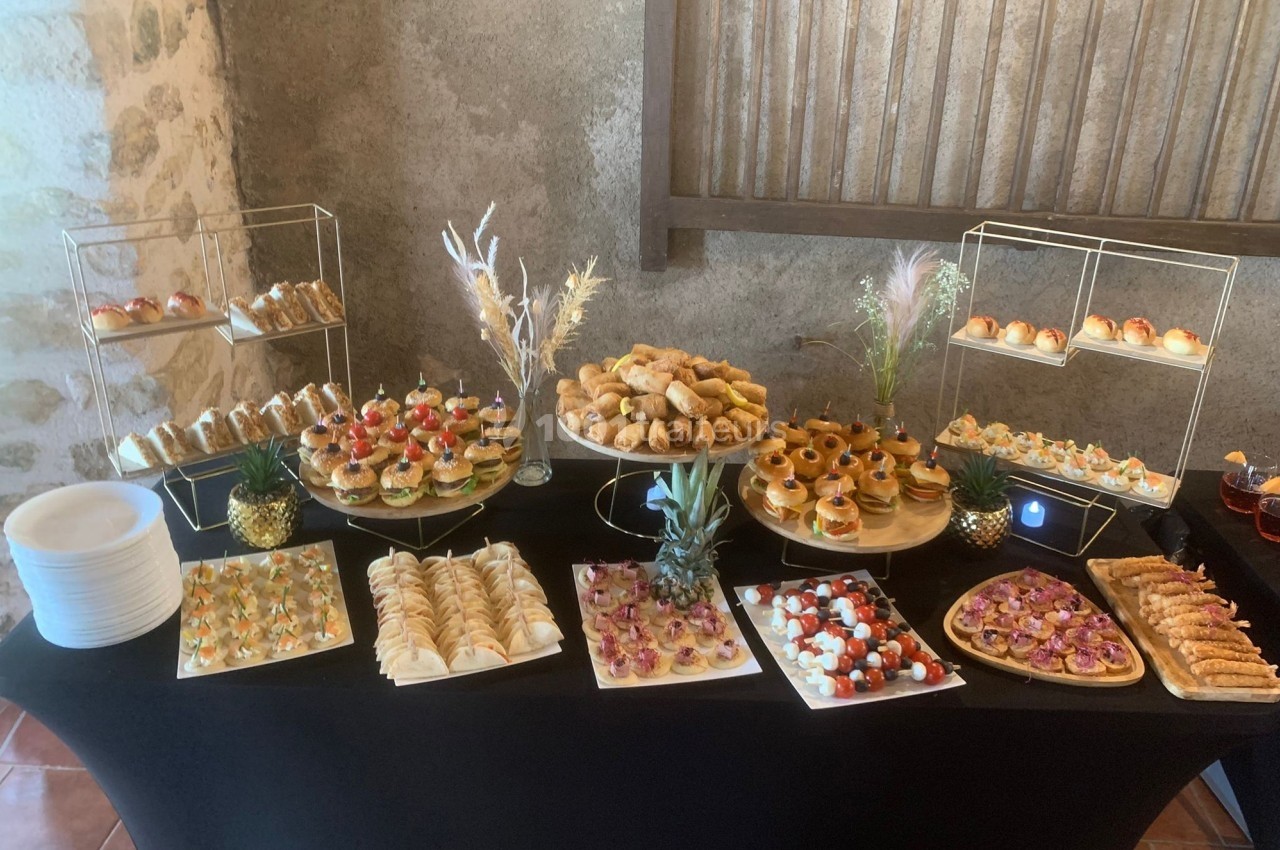 Buffet de pièces cocktail variées comprenant canapés, mini-sandwichs, viennoiseries et amuse-bouches sur une table noire.