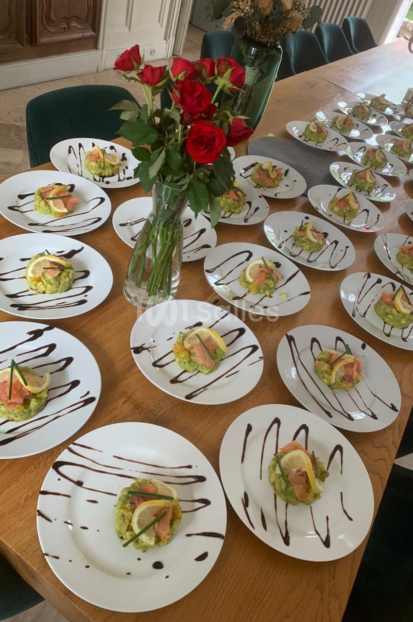 Assiettes dressées avec des entrées à base de saumon, avocat et citron, disposées sur une grande table en bois.