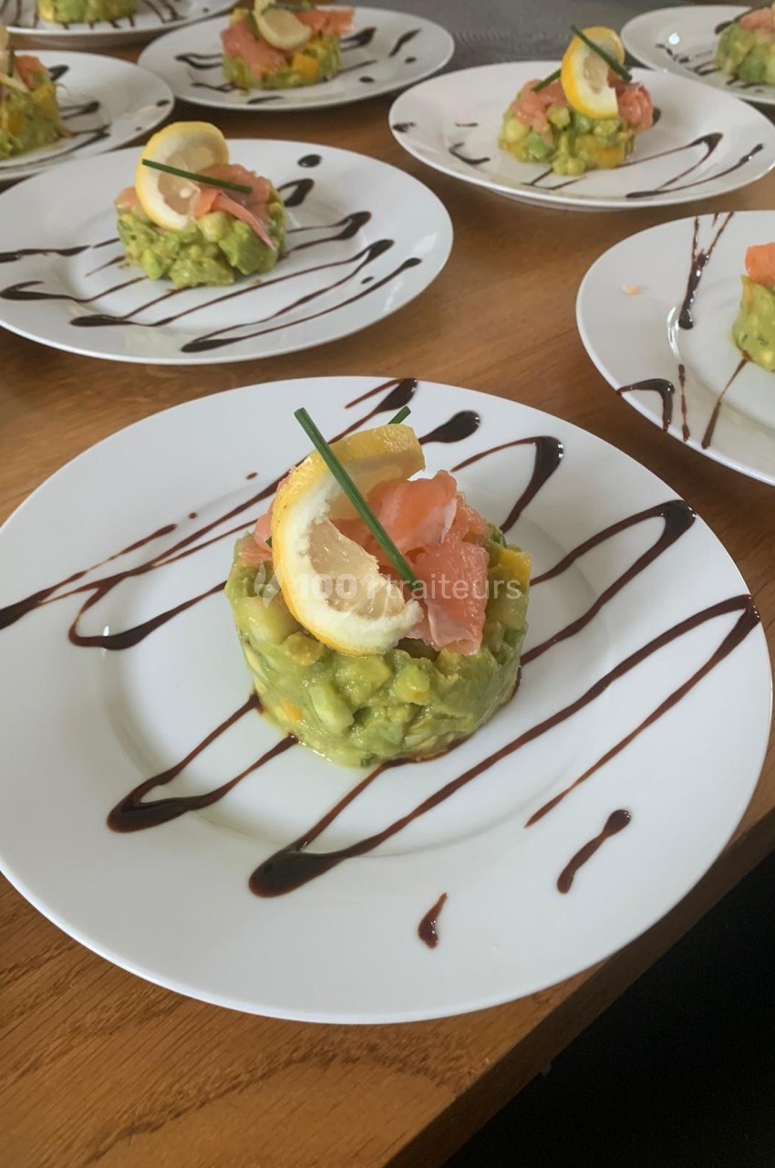 Assiette contenant un tartare d'avocat garni de saumon fumé, citron et ciboulette, décorée de filet de sauce balsamique.