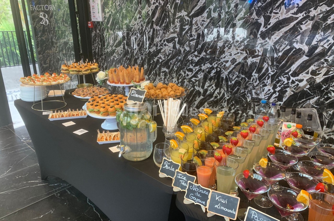 Buffet avec boissons fruitées, verrines, pâtisseries et snacks salés disposés sur une table noire dans un décor moderne.