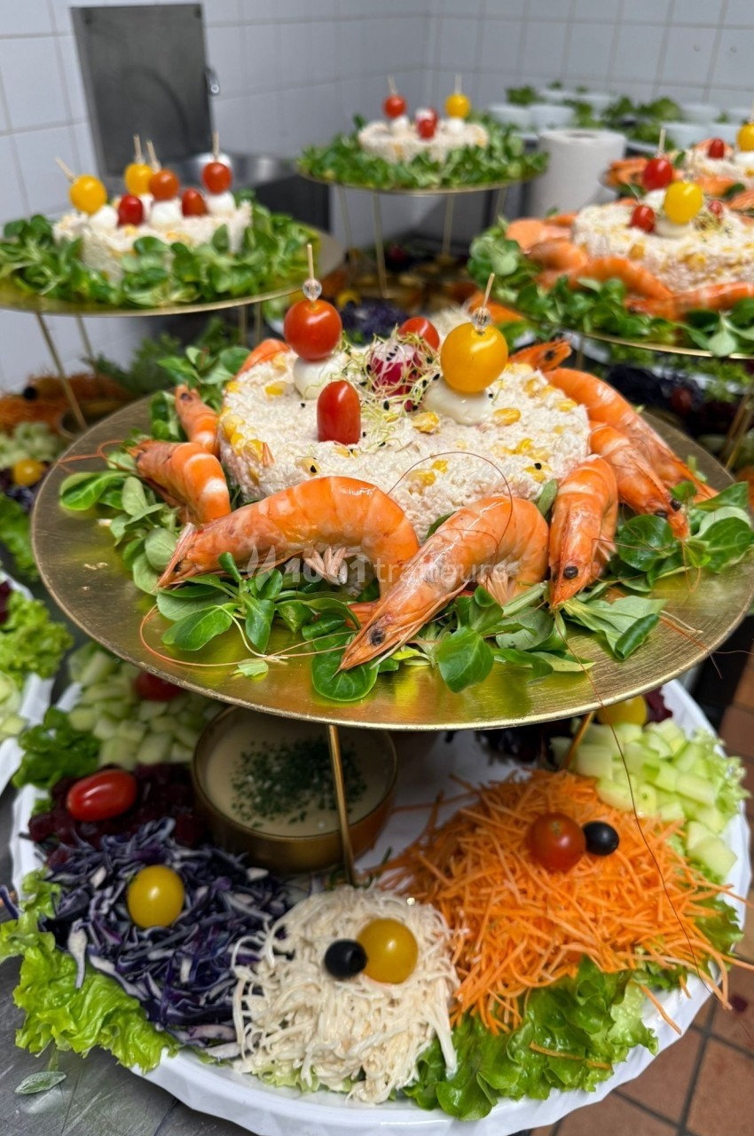 Plateaux garnis de salades, crevettes, légumes frais et décorations colorées, présentés sur des supports dorés.