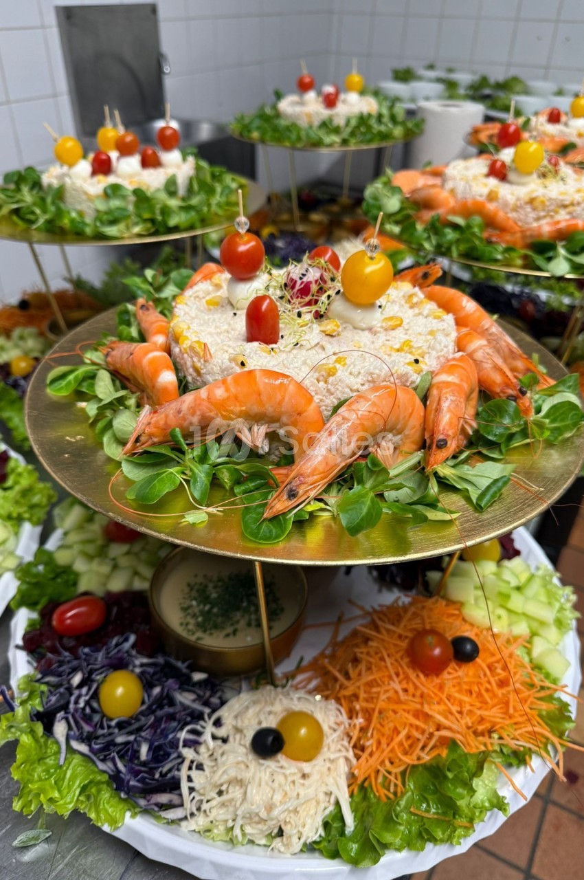 Plateaux garnis de salades, crevettes, légumes frais et décorations colorées, présentés sur des supports dorés.