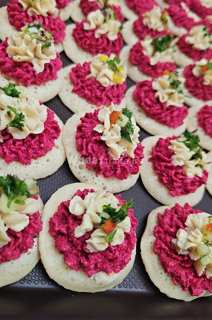 Plateau de mini-blinis garnis de mousse rose, crème décorative et herbes fraîches.