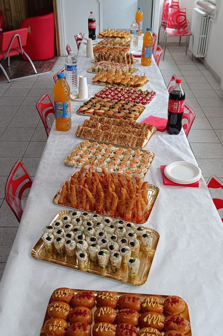 Buffet composé de pâtisseries, sushis, feuilletés et boissons, disposé sur une longue table blanche.