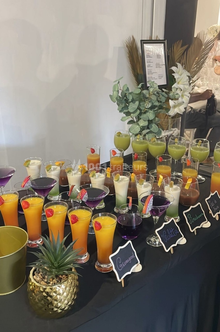 Buffet de cocktails colorés variés sur une table noire, décorée avec des plantes et des étiquettes indiquant les saveurs.