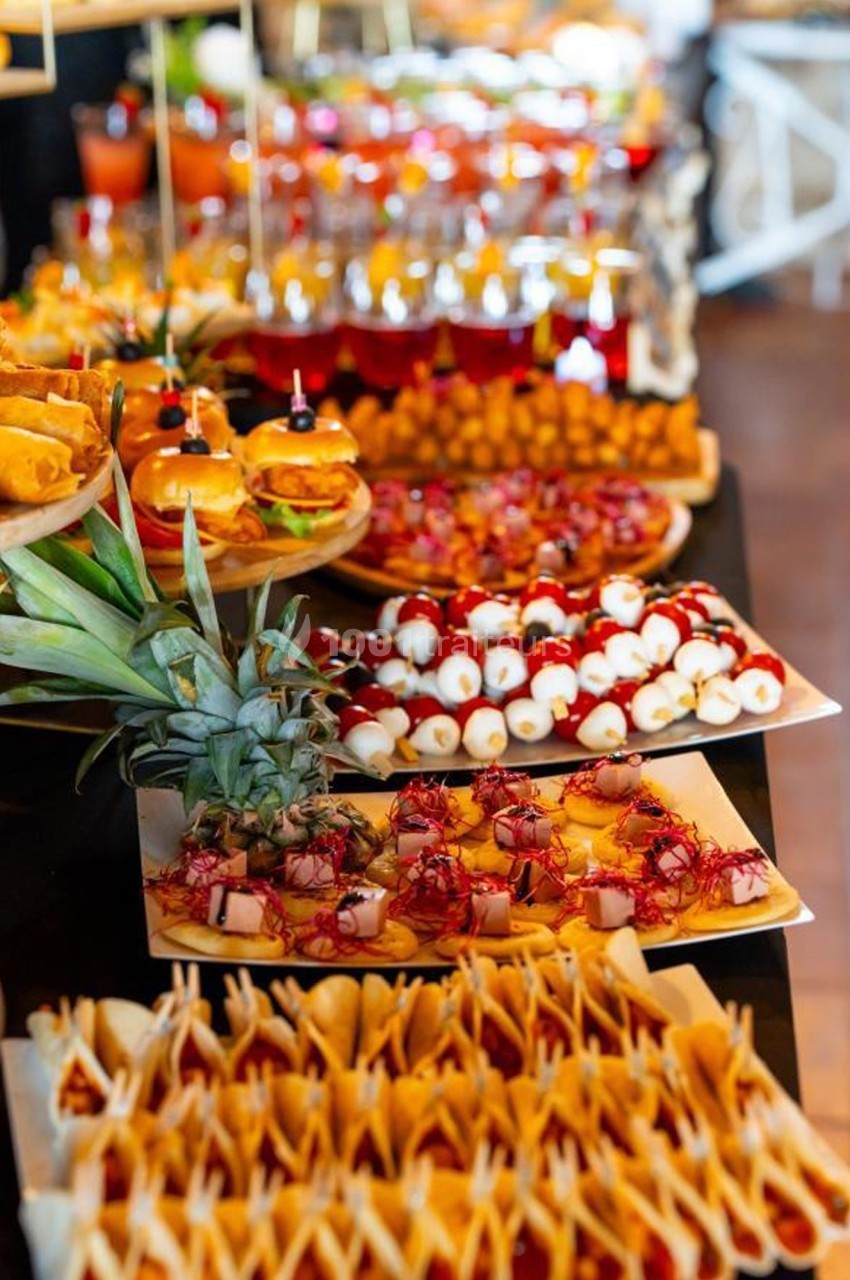 Buffet coloré avec divers plats, dont brochettes, mini-burgers, fruits et amuse-bouches sur une table.