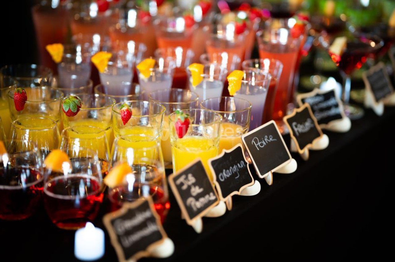 Verres de cocktails colorés alignés sur une table, étiquetés avec des ardoises indiquant leurs noms.