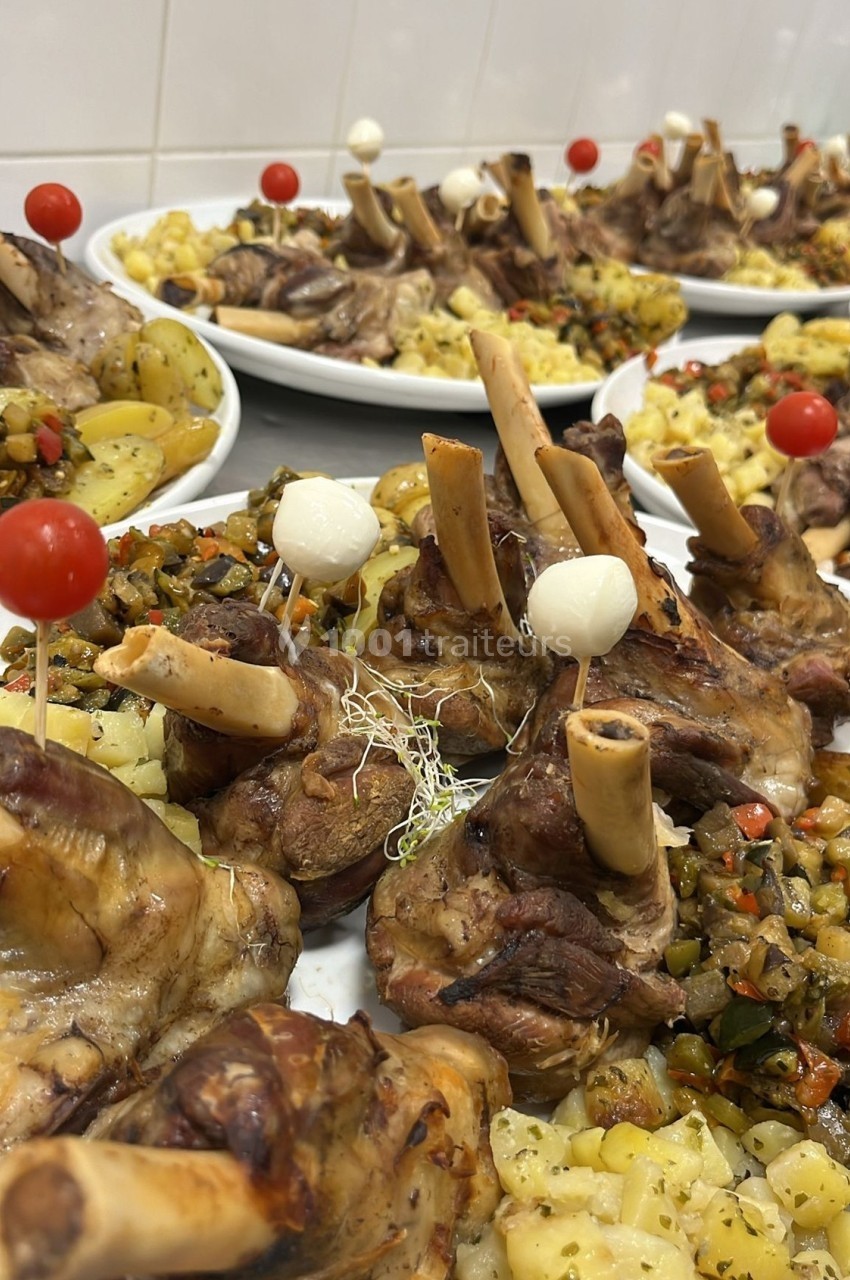 Assiettes de jarrets d'agneau rôtis accompagnés de légumes sautés et pommes de terre, décorées de tomates cerises et oignons.