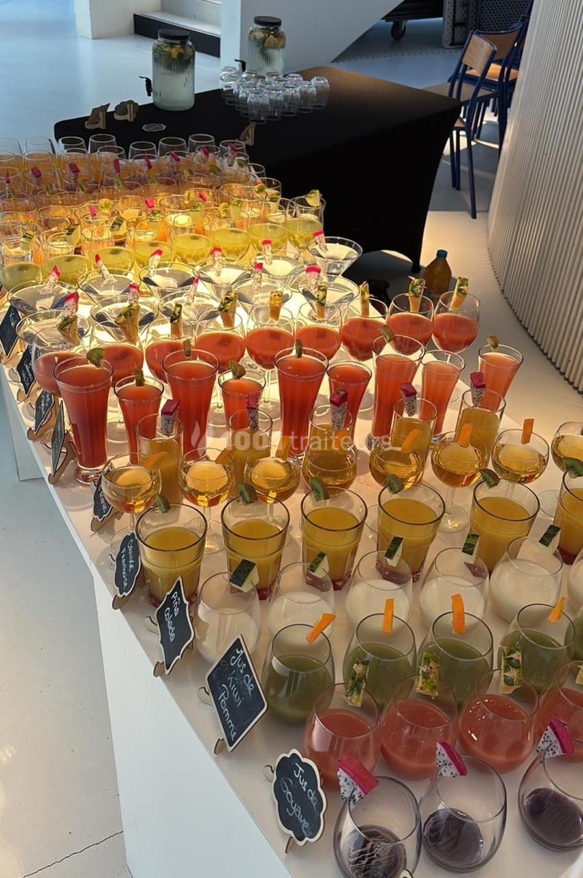 Buffet de cocktails colorés disposés sur une table blanche, avec étiquettes indiquant les saveurs.