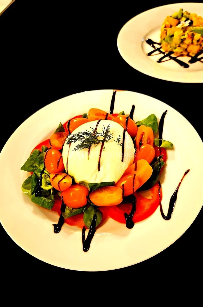 Assiette de burrata avec tomates cerises, feuilles de salade et filet de vinaigre balsamique.