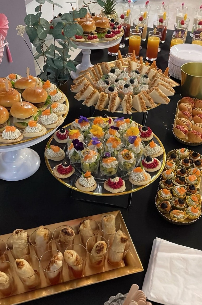 Buffet avec une variété de bouchées salées et sucrées, incluant sandwichs, verrines, feuilletés et jus de fruits.