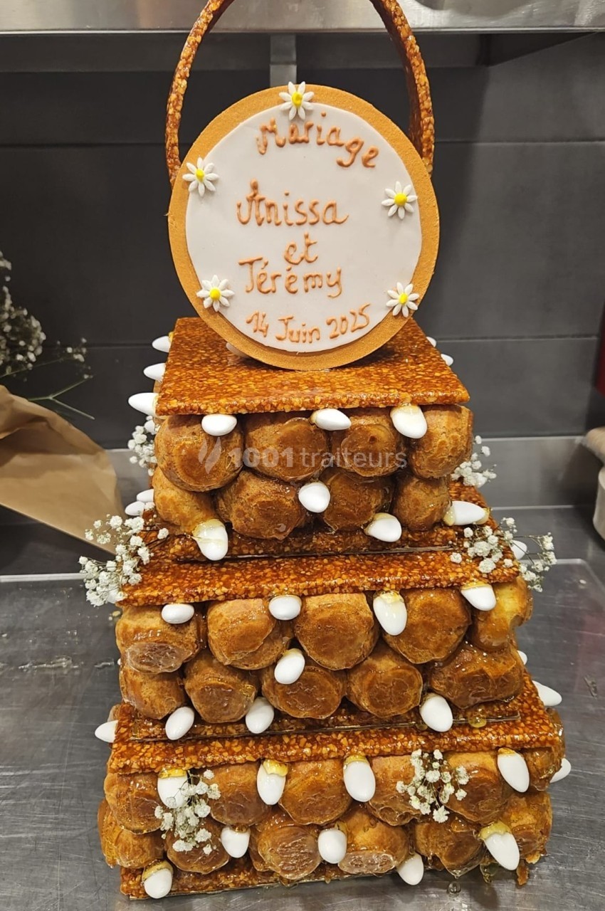 Pièce montée en choux décorée de fleurs et d'amandes, avec une plaque indiquant ’Mariage Anissa et Jérémy, 14 Juin 2025’.