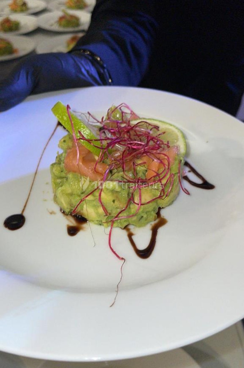Entrée composée d'avocat, saumon fumé, germes rouges et rondelle de citron, décorée de sauce balsamique.