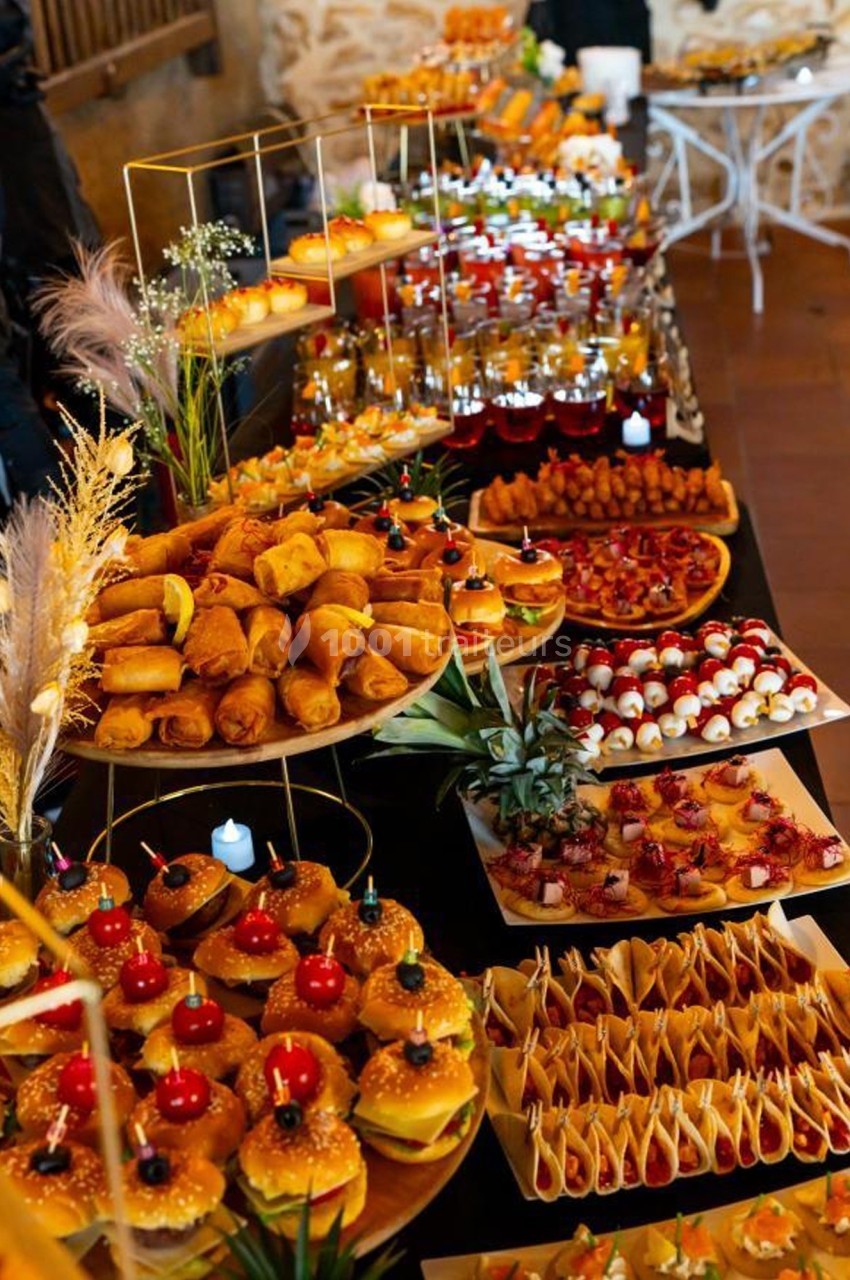Buffet varié avec mini-burgers, rouleaux, verrines, brochettes et autres amuse-bouches disposés sur des plateaux.