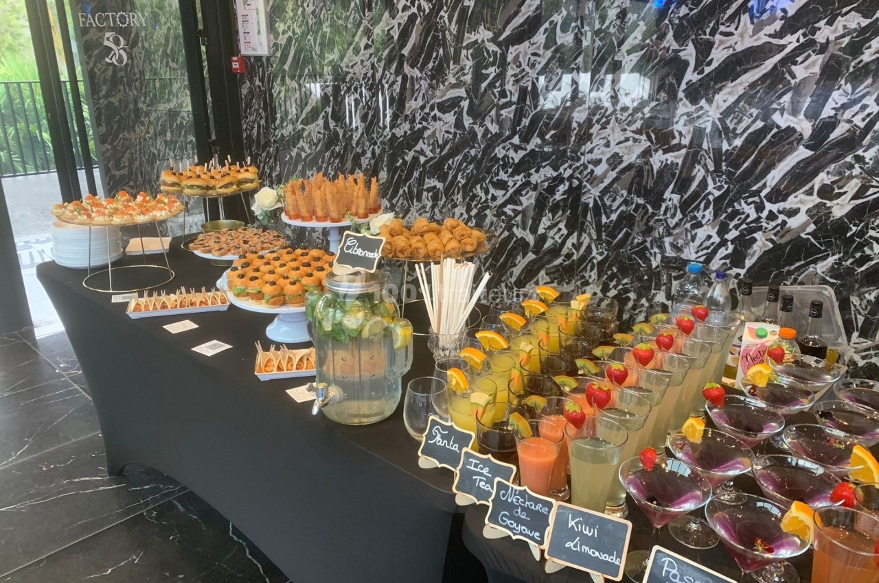 Buffet avec boissons fruitées, verrines, pâtisseries et snacks salés disposés sur une table noire devant un mur marbré.
