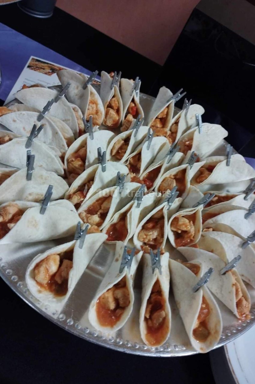 Plateau de mini-tacos garnis de poulet et sauce, maintenus par des pinces, présenté sur une table.