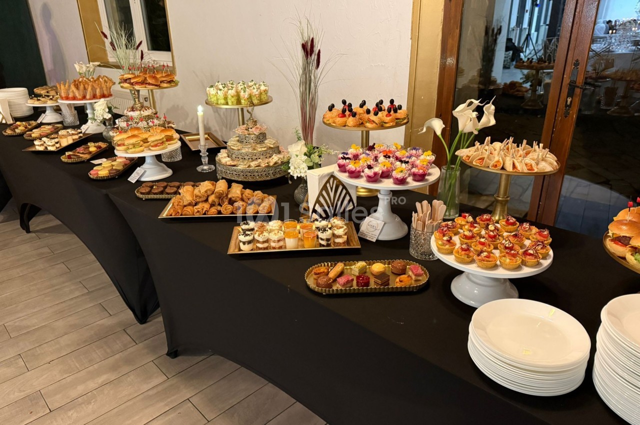 Buffet de desserts et amuse-bouches variés disposés sur des tables noires avec présentoirs et décorations florales.