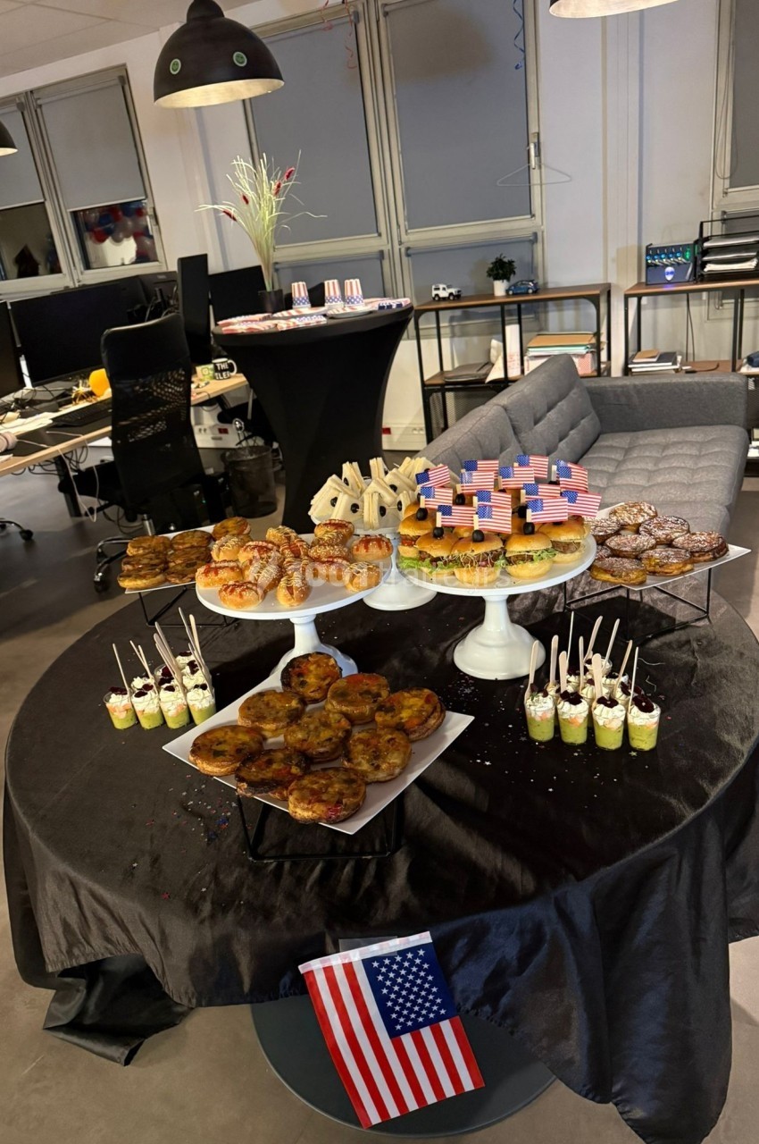 Table garnie de desserts variés, décorés aux couleurs des États-Unis, dans un espace de bureau moderne.