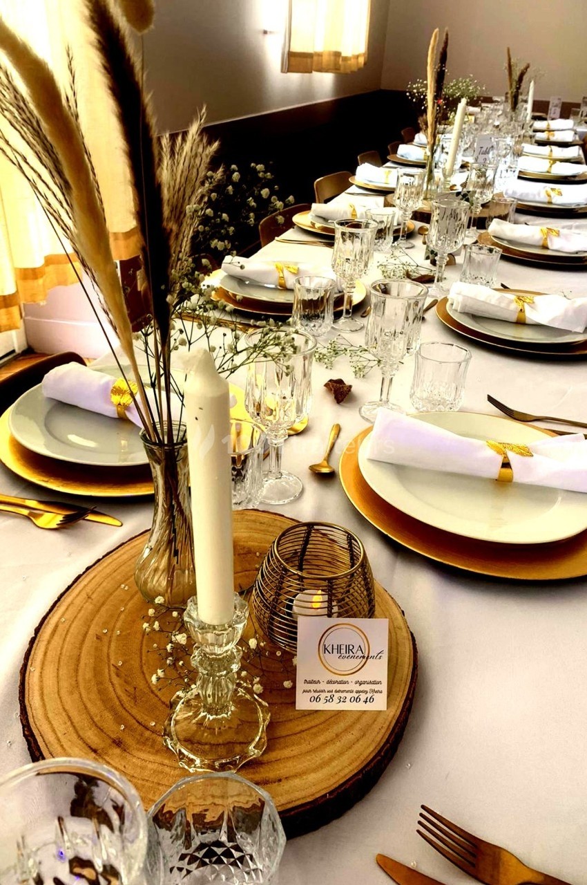 Table élégamment dressée avec des assiettes blanches, des couverts dorés, des bougies et des décorations naturelles.