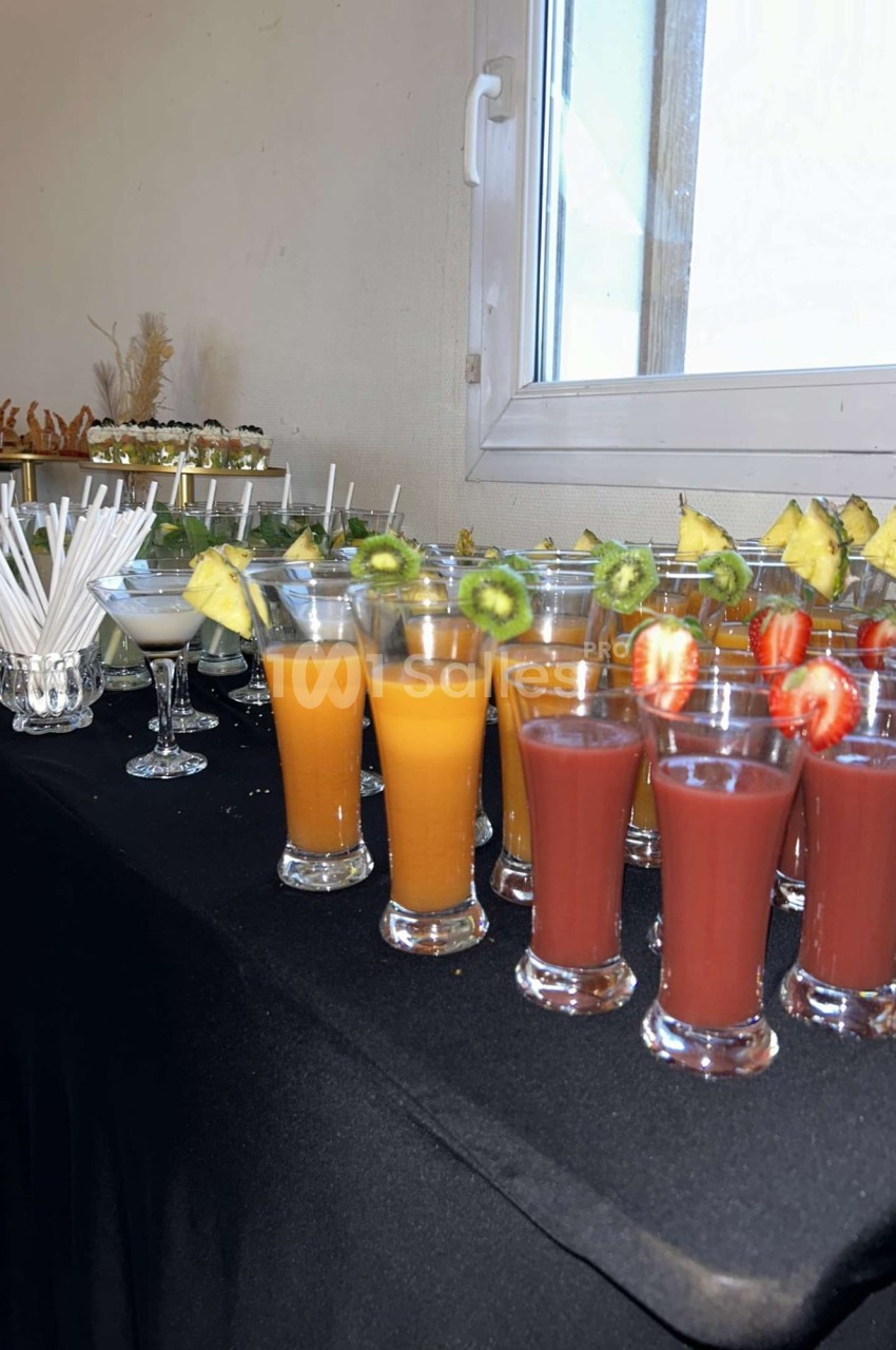 Verres de jus de fruits variés avec des garnitures de fruits frais, disposés sur une table recouverte d'une nappe noire.