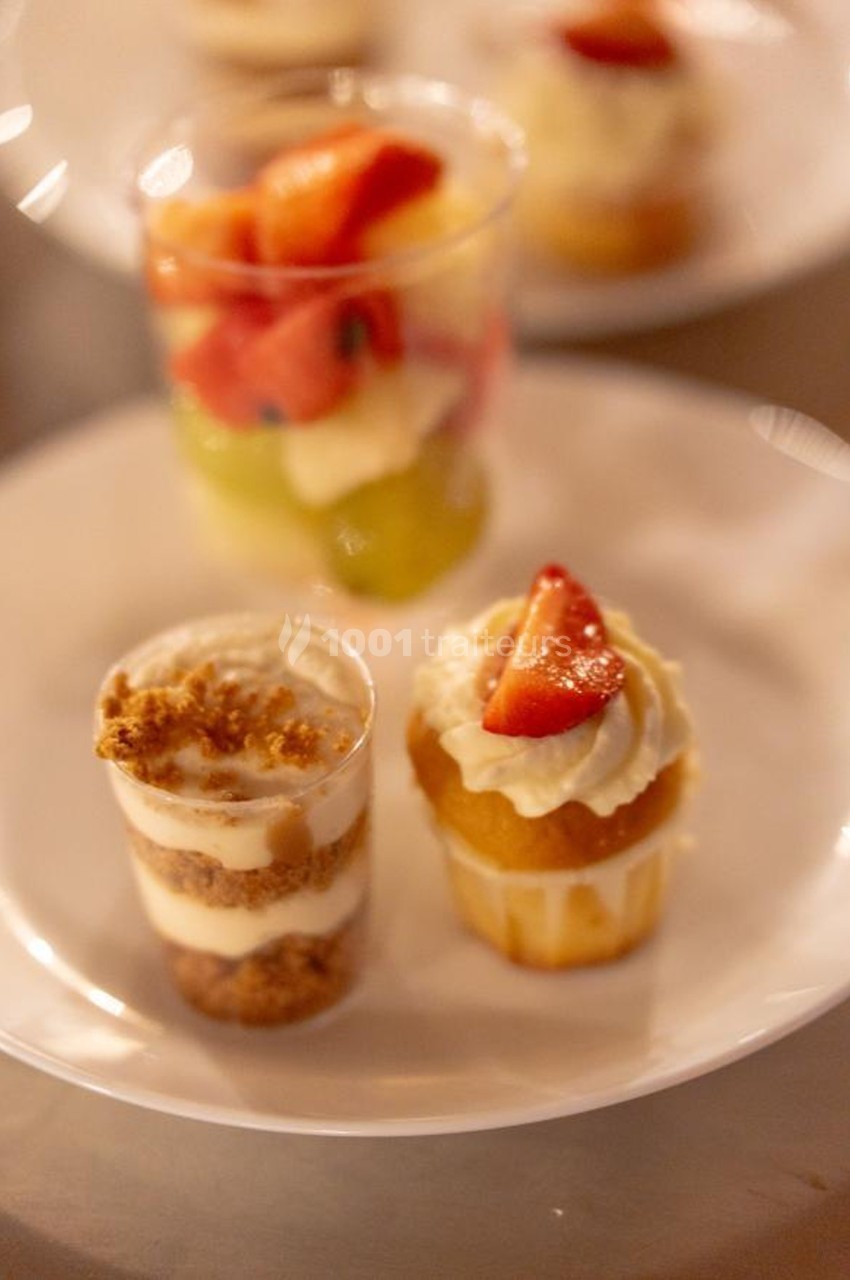 Deux desserts sur une assiette : une verrine avec crumble et une mini-cupcake décorée de chantilly et fraise.