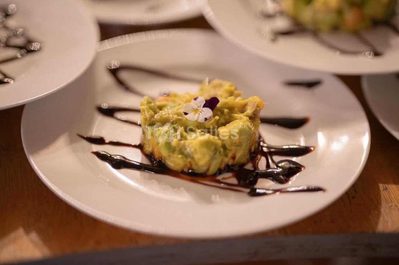 Assiette contenant une préparation d'avocat décorée de fleurs comestibles et de traits de sauce balsamique.