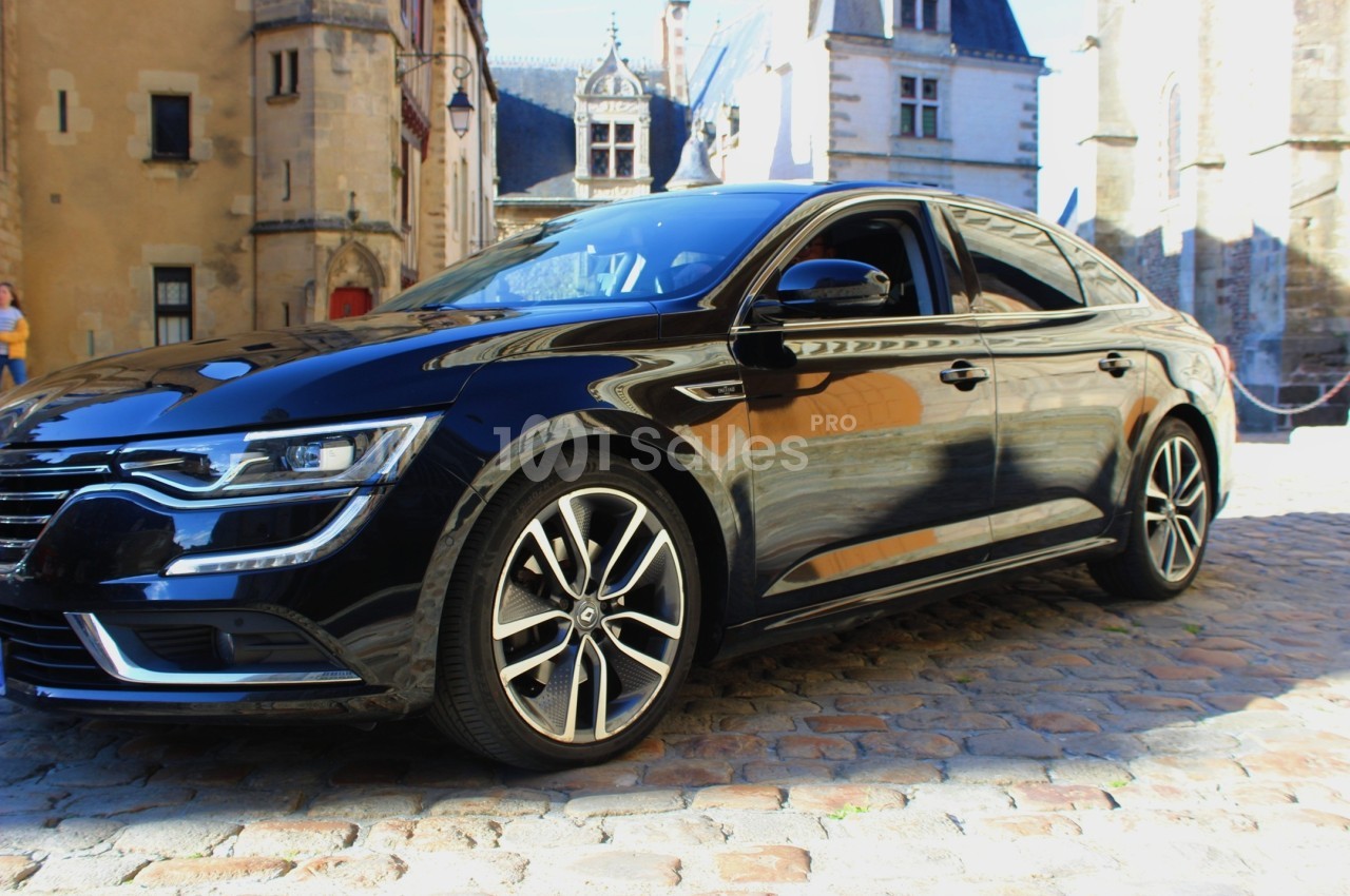 Voiture noire garée sur une place pavée, entourée de bâtiments historiques en arrière-plan.