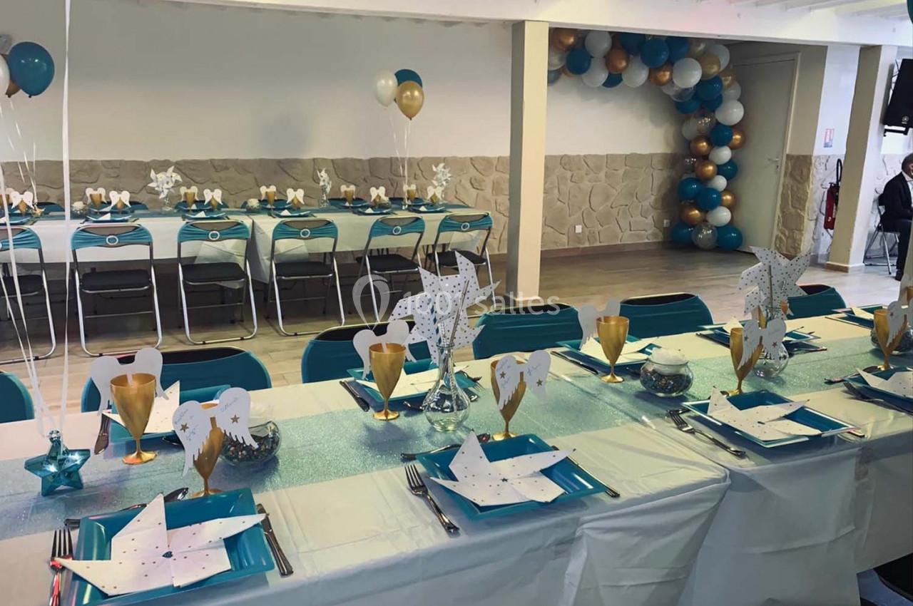 Salle décorée pour un événement avec tables dressées, nappes turquoise et blanche, ballons et éléments festifs.
