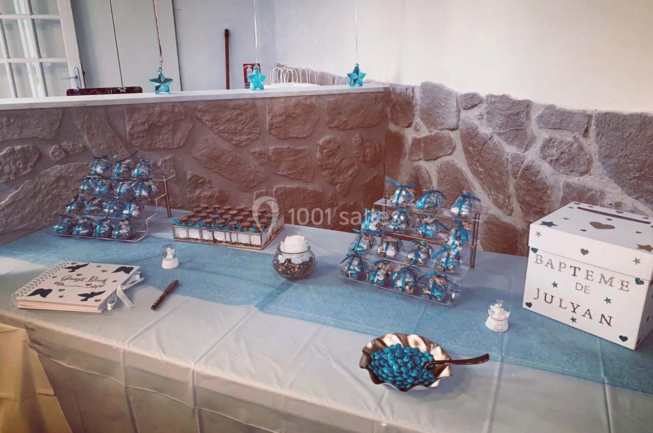 Table décorée pour un baptême avec des friandises bleues, une urne blanche et des éléments de décoration étoilés.